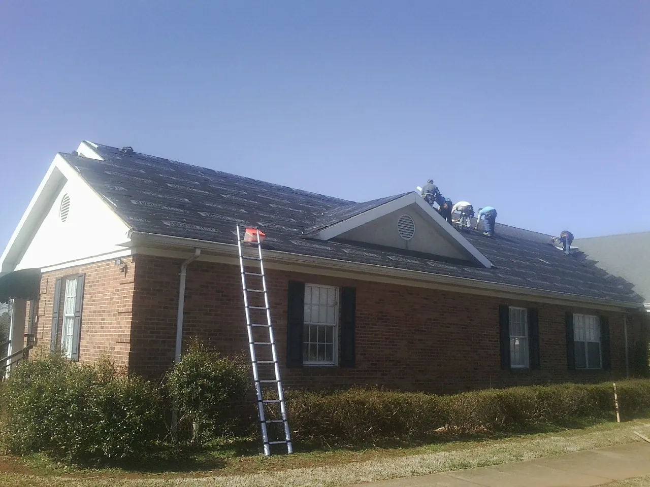 Crew tearing shingles off a brick ranch roof with a ladder set — Metal Roof Repair work by our crew in Galt