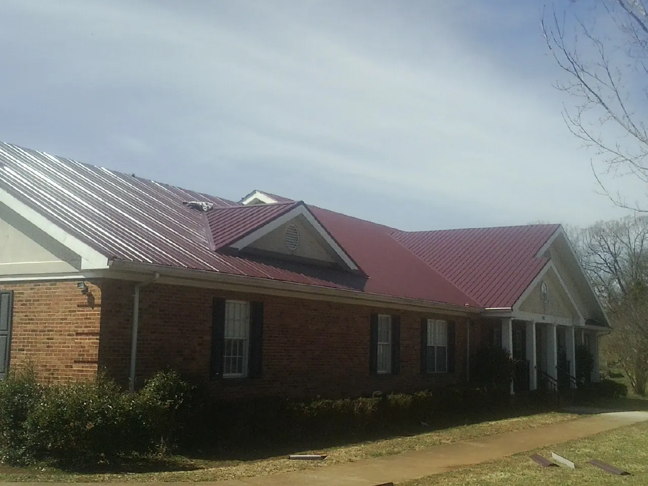 Red metal roof with gabled entries on a long brick building, from a Hail Damage Roof Repair job in Galt