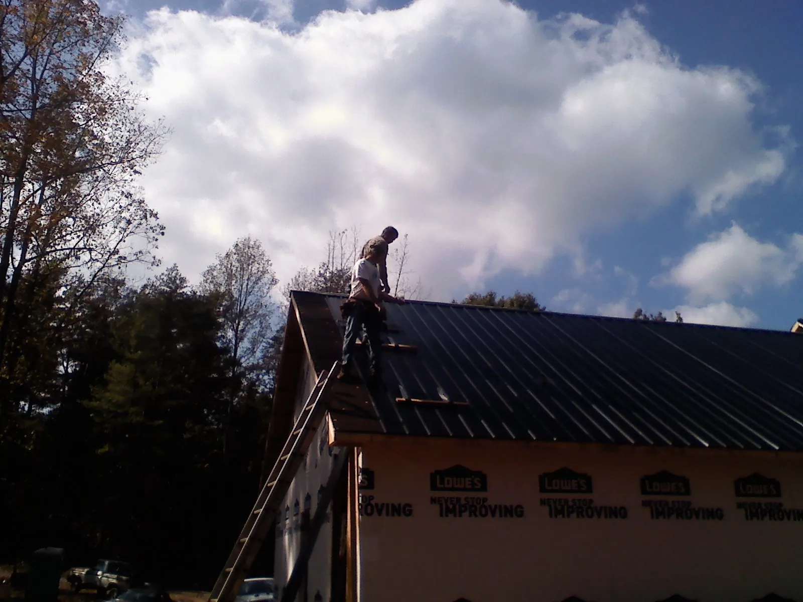 Roofer fastening dark metal panels high against a cloudy sky, from a Roof Inspection job in Galt
